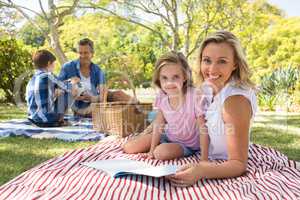 Mother and daughter reading book while father and son playing with football in park