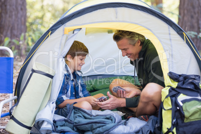 Happy father and son sitting inside tent in forest