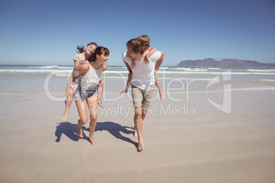 Happy parents piggybacking their children at beach