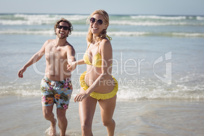 Happy young couple running on shore at beach`