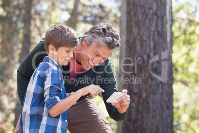 Cheerful father and son using mobile phone in forest