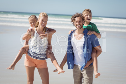 Portrait of happy parents piggybacking their children at beach