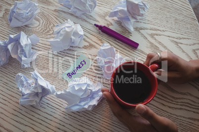 Hand of businesswoman holding coffee by crumpled papers on desk in office