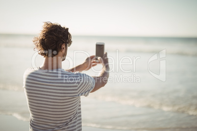 Rear view of man photographing sea at beach