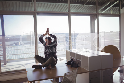 Young businessman meditating on desk at office
