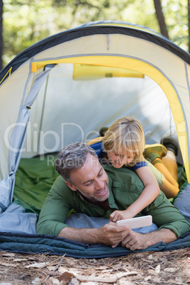 Happy father and son enjoying while using mobile phone at campsite