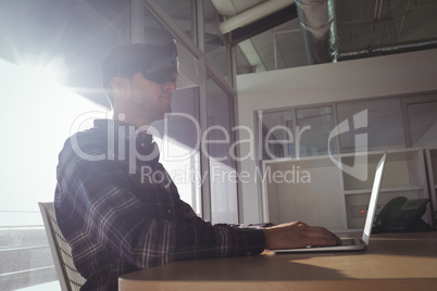 Businessman wearing virtual reality headset while using laptop in office