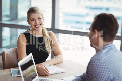 Portrait of smiling executive sitting with her colleague at desk
