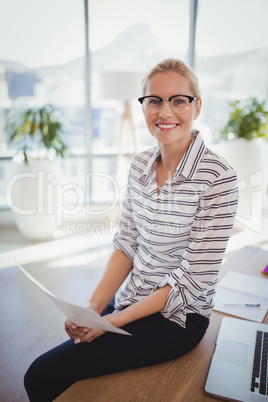 Portrait of smiling executive holding document at desk