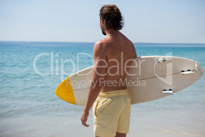Surfer with surfboard looking at sea from the beach