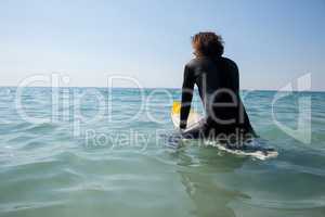 Surfer sitting on surfboard at seacoast