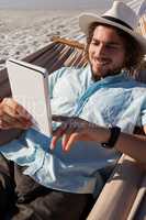 Man relaxing on hammock and using digital tablet on the beach