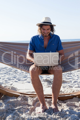 Man using laptop while sitting on hammock at beach