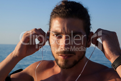Muscular man listening to music on headphones at beach