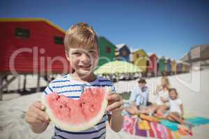 Portrait of smiling boy holding watermelon with family in background
