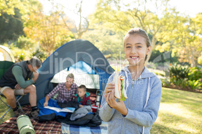 Smiling girl holding a sandwich while family sitting outside the tent