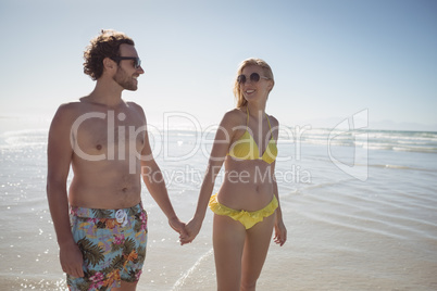 Happy young couple holding hands at beach during sunny day