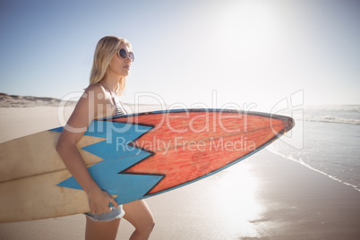 Woman carrying surfboard at beach during sunny day