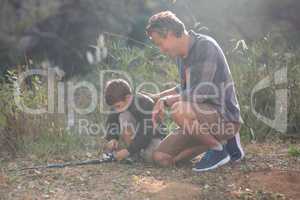 Father and son with fishing rod kneeling on field