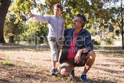 Happy man looking at boy pointing away in forest