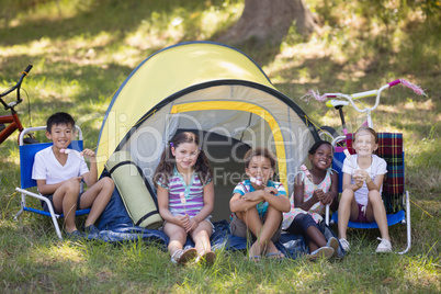 Cheerful children sitting outside tent at campsite