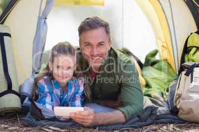 Father and daughter using mobile phone while resting in tent