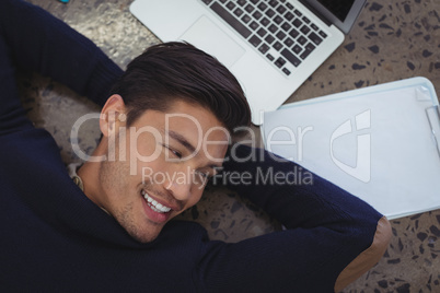 Smiling businessman lying by laptop and clipboard at office