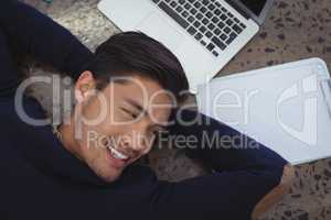 Smiling businessman lying by laptop and clipboard at office