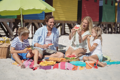 Happy family eating watermelon while sitting together at beach