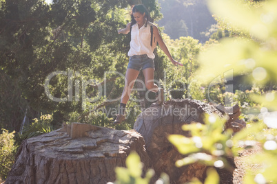 Female hiker jumping from tree stumps in forest