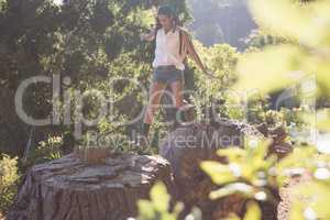 Female hiker jumping from tree stumps in forest