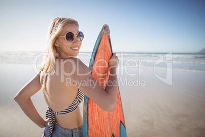 Portrait of smiling woman holding surfboard at beach