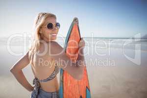 Portrait of smiling woman holding surfboard at beach
