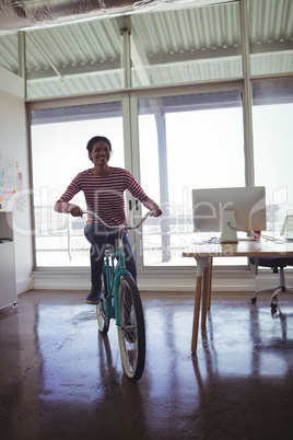 Confident businesswoman riding bicycle in creative office