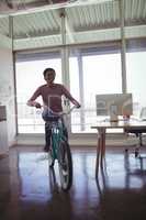 Confident businesswoman riding bicycle in creative office
