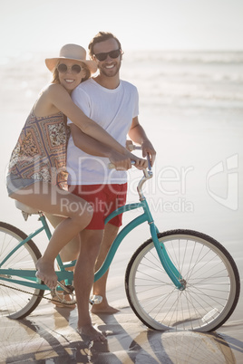 Portrait of smiling couple with bicycle on shore at beach