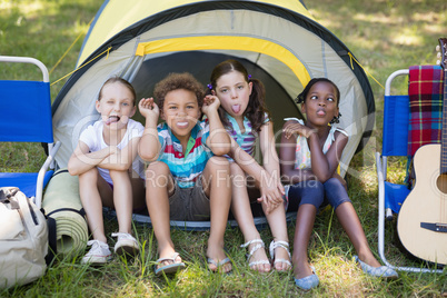 Children making face while sitting in tent at campsite