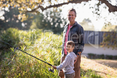 Portrait of father standing by boy holding fishing rod