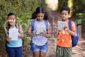 Boys and girls using digital tablets at natural parkland