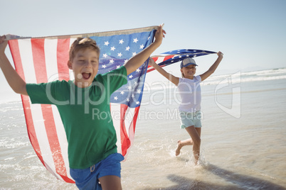 Happy siblings holding American flags while running on shore