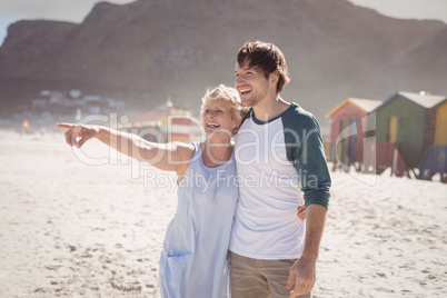 Happy woman pointing away with her son standing at beach