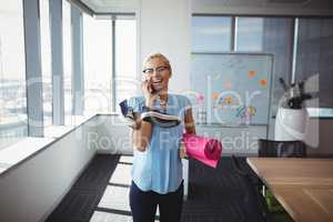 Smiling executive talking on mobile phone while holding exercise mat and shoes