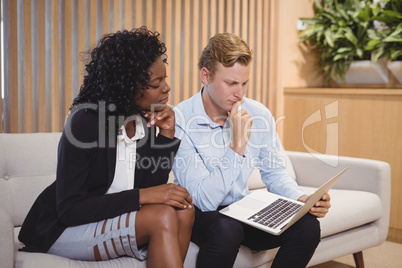 Attentive executives sitting on sofa and using laptop