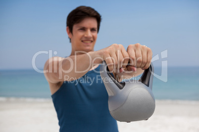 Young man holding kettlebell at beach