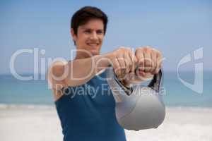 Young man holding kettlebell at beach