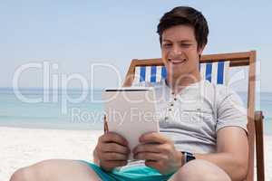 Man sitting on sunlounger and using digital tablet on the beach