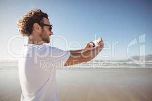 Happy man taking selfie against blue sky at beach