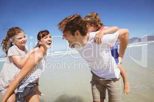 Cheerful parents piggybacking their children at beach
