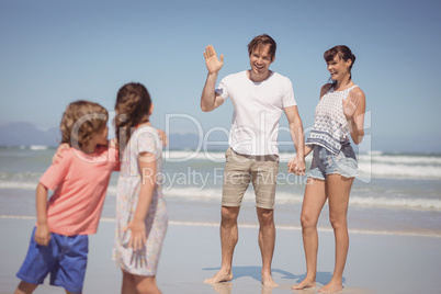 Happy parents waving hands while looking at children standing on shore