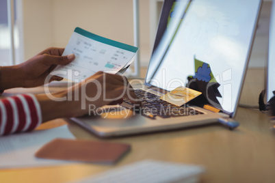 Businesswoman holding documents while using laptop in office